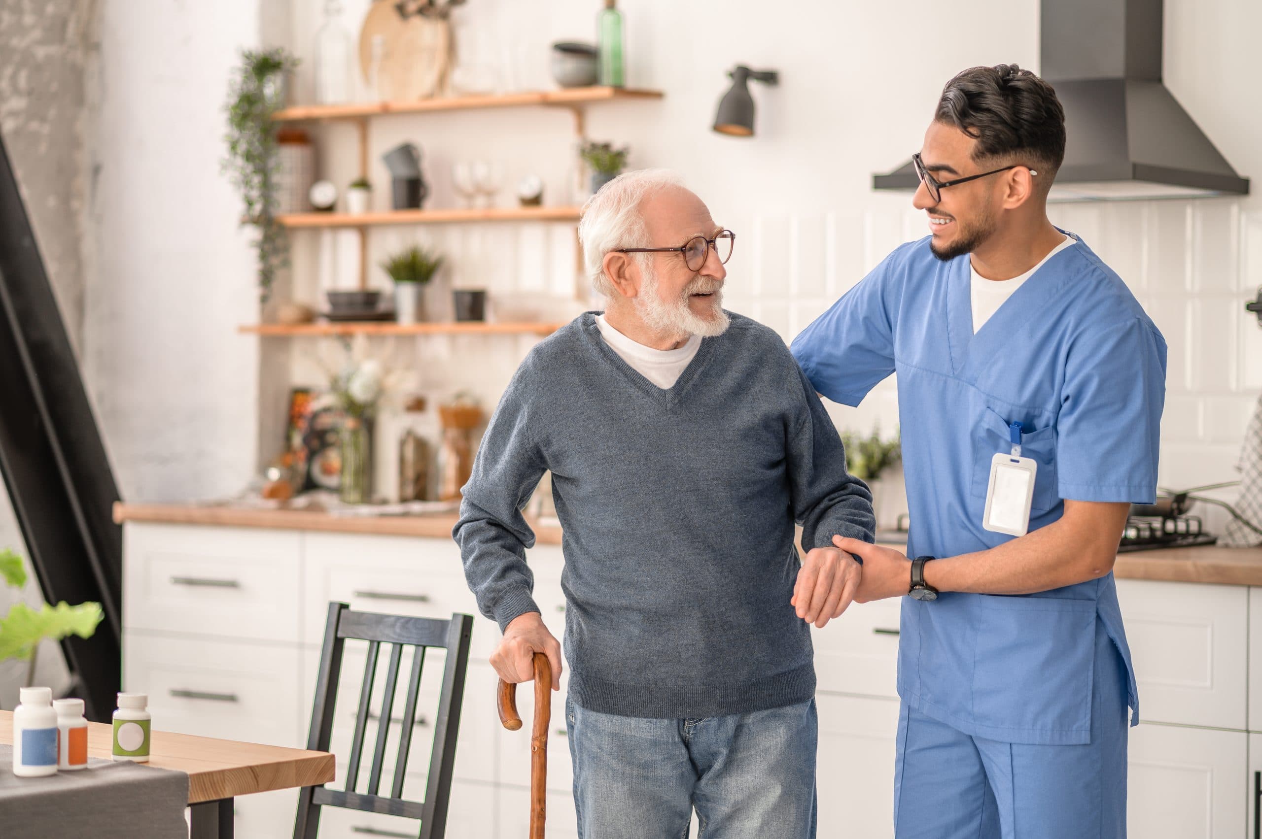 A carer supporting an older man as he walks in his kitchen