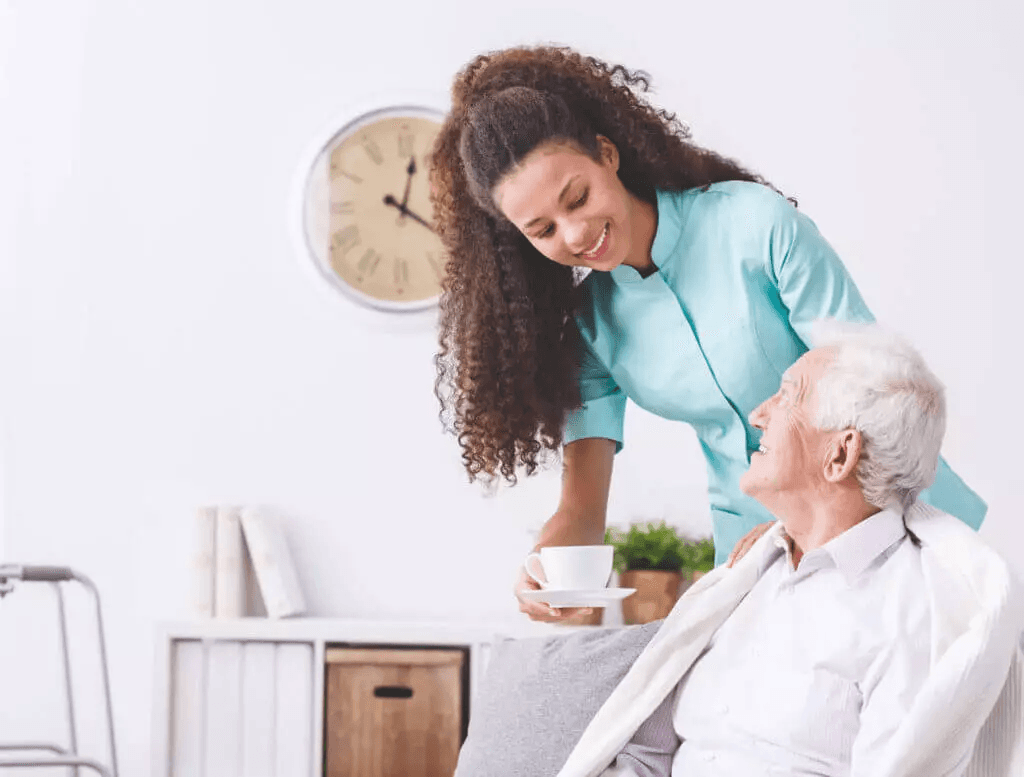 A carer bringing a warm drink to a smiling older man at home